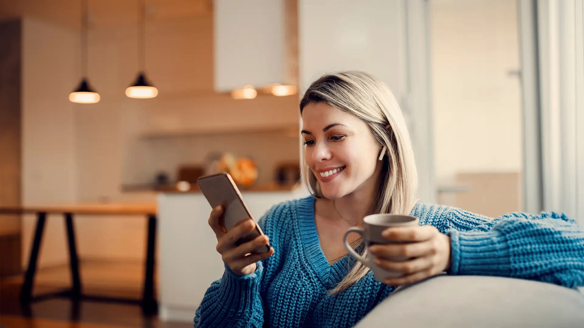 Eine lächelnde Frau die zuhause auf Ihrem Sofa auf Ihr Smartphone schaut